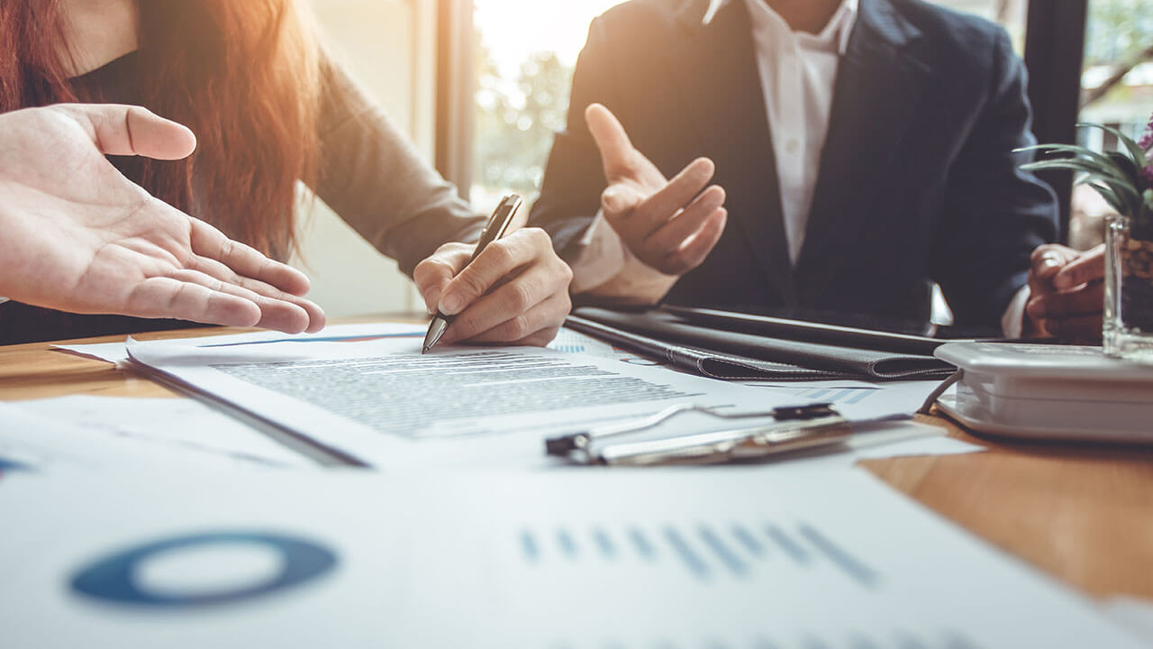 Close up of people sitting around table while one person signs a document